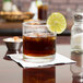A Libbey Lexington old fashioned glass of brown liquid with ice and a lime wedge.
