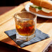 A Libbey Inverness rocks glass filled with brown liquid and ice on a table next to a sandwich.