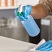 A person in blue gloves using a Lavex spray bottle to disinfect a table.