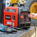 A hand plugging a black power cord into the Tomahawk Inverter Series portable power generator.