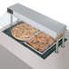 A countertop with a pizza and chicken in trays on a Hatco built in heated shelf.