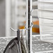 A silver Regency chrome all-purpose hook holding a pair of oven mitts on a metal pole.