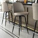 Three Lancaster Table & Seating Black Swivel Barstools with gray vinyl bucket seats at a bar.