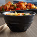 A black melamine bowl filled with rice with chopsticks on a table.