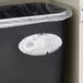 A black Fresh Products Curve air freshener holder on a trash can with a plastic bag and a white shoe on the side.
