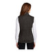 A woman wearing a black heather Port Authority fleece sweater vest.