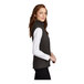 A woman wearing a black heather Port Authority fleece sweater vest.