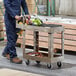 A man in blue overalls is pushing a Rubbermaid beige utility cart with tools on it.