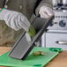 A gloved hand uses Emperor's Select large plastic mandoline to slice a cucumber.