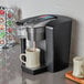 A Keurig K-1550 commercial single serve pod coffee maker on a counter with a cup in it.