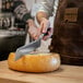 A person cutting a wheel of cheese with a Boska stainless steel cheese knife.