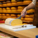 A person using a Boska Stainless Steel Semi-Hard Cheese Knife to cut cheese on a cutting board.