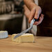 A person using a Boska stainless steel cheese knife to cut a piece of cheese.