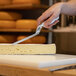 A person using a Boska stainless steel soft cheese knife to cut cheese on a cutting board.