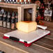 A large block of cheese on a Boska Cheese-O-Matic cutter on a cutting board.