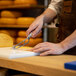 A person cutting cheese with a Boska stainless steel cheese knife on a cutting board.