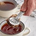 A person using Fox Run stainless steel tea bag tongs to hold a tea bag over a cup of tea.