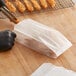 A person using tongs to hold fried shrimp in a Kari-Out glassine bag.