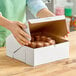 A person opening a Southern Champion white bakery box on a counter to reveal cake.