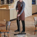 A man in an apron using a Vikan black single blade rubber floor squeegee with a long handle to clean a floor.