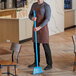 A man in an apron sweeping the floor with a Vikan blue broom head.