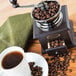 A Fox Run coffee handgrinder with coffee beans and a cup of coffee on a table.