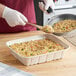 A person holding a World Centric compostable fiber catering pan filled with rice and a wooden spoon.