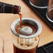 A person using an Outset Stainless Steel Black and Tan Layering Tool to pour a beer into a glass of liquid.