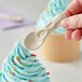 A hand holding a World Centric compostable fiber tasting spoon over a blue frosted cupcake.