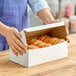 A person holding a Southern Champion white donut box on a table with donuts inside.