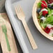 A World Centric compostable bamboo fork wrapped in paper next to a bowl of salad.