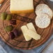 An Ironwood acacia wood round serving board with "Fromage" engraving holding cheese and crackers.