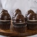 A chef holding a wood tray of chocolate cupcakes with Ghirardelli Dark Coating on top.
