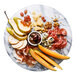 A white marble lazy susan with a plate of cheese, fruit, and crackers.