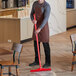 A man in an apron using a red Vikan Ultra-Hygienic floor squeegee to clean a floor.