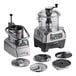 A commercial food processor set with a clear plastic bowl, continuous feed attachment, and multiple stainless steel discs.