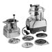 A commercial food processor set with a clear plastic bowl, continuous feed attachment, and multiple slicing and dicing discs.