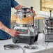 A commercial food processor with a clear plastic bowl and digital controls, shown in use on a kitchen counter.
