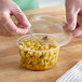 A person wearing plastic gloves putting food into a Choice clear plastic deli container.