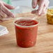 A person putting salsa into a Choice plastic deli container with a lid.