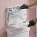 A person putting a Scott Pro white paper toilet seat cover on a dispenser.