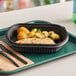 A brown tray with a black rectangular Pactiv container filled with food and black plastic utensils.