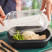 A person holding a clear plastic Pactiv container with food in it.