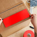 A person's hands cutting a red rectangular Lavex inventory label from a roll.