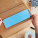 A person's hands using scissors to cut a rectangular sky blue paper label.