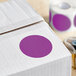 A white box with purple circle stickers on it and a roll of purple and white paper with a purple label.