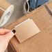 A hand holding a Lavex rectangular brown paper label on a roll in a cardboard box.