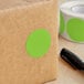 A brown box with a roll of Lavex semi-gloss green inventory labels with a green circle on it next to a black pen.