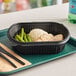 A black Pactiv MealMaster container with food on a tray with a black knife and fork.
