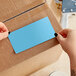 A person's hands holding a rectangular sky blue paper label.